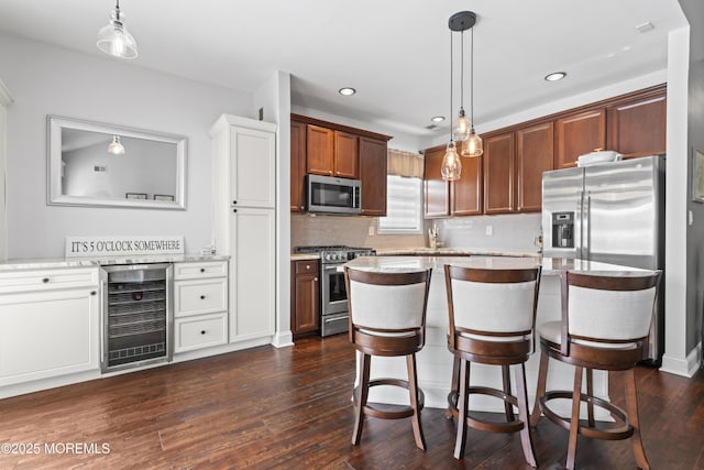 kitchen featuring decorative light fixtures, a breakfast bar area, beverage cooler, stainless steel appliances, and dark wood-type flooring