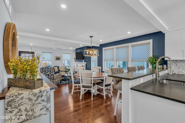 kitchen featuring sink, a breakfast bar area, white cabinetry, hanging light fixtures, and dark hardwood / wood-style flooring