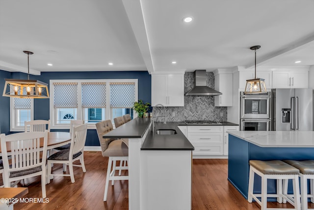 kitchen featuring pendant lighting, wall chimney exhaust hood, stainless steel appliances, and white cabinets