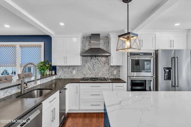 kitchen featuring wall chimney exhaust hood, stainless steel appliances, decorative light fixtures, and white cabinets