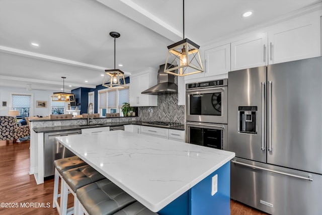 kitchen with wall chimney range hood, sink, appliances with stainless steel finishes, hanging light fixtures, and a kitchen island