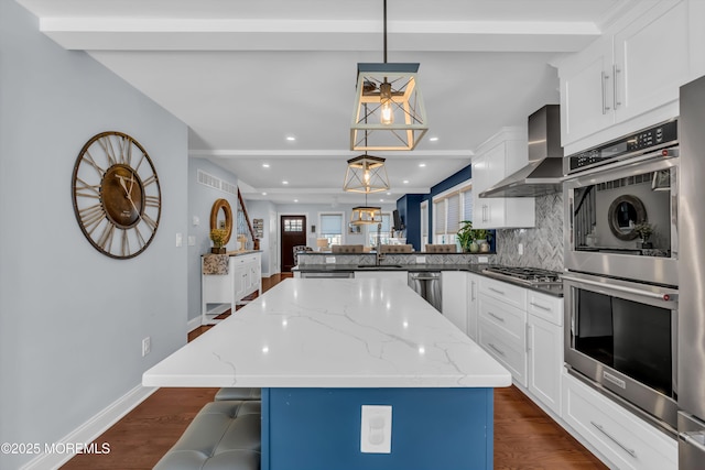 kitchen with hanging light fixtures, a center island, light stone counters, kitchen peninsula, and wall chimney exhaust hood