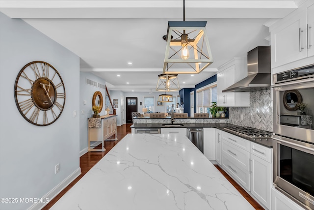 kitchen with pendant lighting, wall chimney range hood, white cabinetry, and dark stone countertops