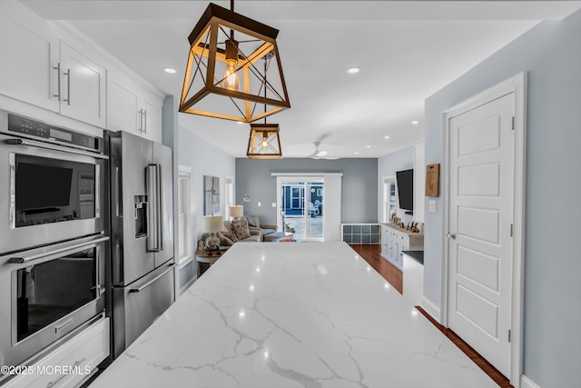 kitchen featuring light stone counters, white cabinetry, decorative light fixtures, appliances with stainless steel finishes, and ceiling fan