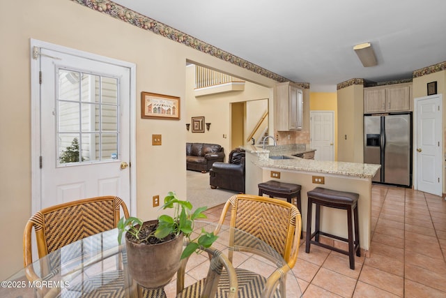 kitchen featuring sink, stainless steel fridge, a breakfast bar, light tile patterned flooring, and kitchen peninsula