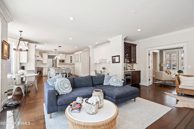 living room featuring bar, dark hardwood / wood-style floors, ornamental molding, beverage cooler, and a chandelier