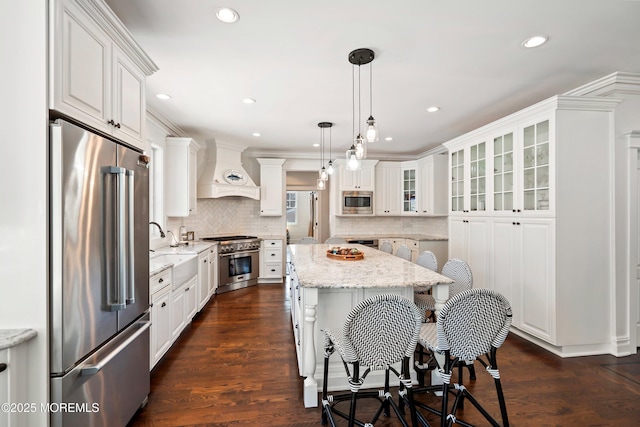 kitchen featuring premium range hood, decorative light fixtures, premium appliances, light stone countertops, and white cabinets