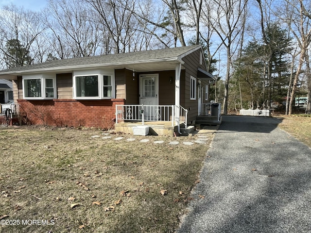 view of front of house featuring a shingled roof, a porch, brick siding, and aphalt driveway