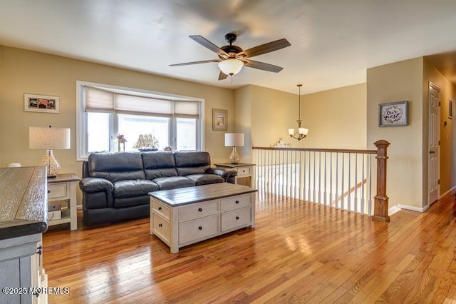 living room featuring ceiling fan with notable chandelier and light hardwood / wood-style flooring