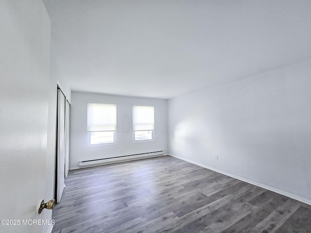 unfurnished room featuring baseboard heating and dark hardwood / wood-style flooring