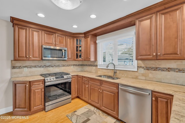 kitchen with sink, light stone counters, tasteful backsplash, light wood-type flooring, and stainless steel appliances