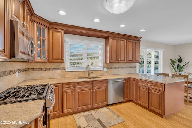 kitchen featuring sink, appliances with stainless steel finishes, tasteful backsplash, kitchen peninsula, and light wood-type flooring