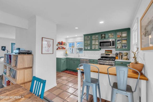 kitchen featuring sink, a breakfast bar, green cabinets, stainless steel appliances, and decorative backsplash