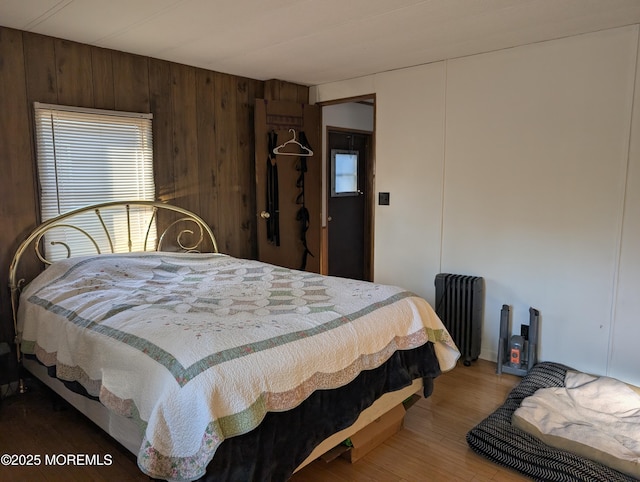 bedroom with wood-type flooring, wooden walls, and radiator