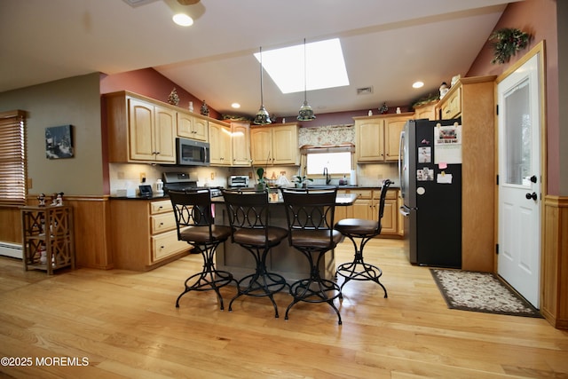 kitchen featuring lofted ceiling with skylight, a breakfast bar, a center island, light wood-type flooring, and appliances with stainless steel finishes