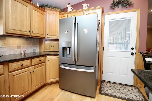 kitchen with light hardwood / wood-style flooring, stainless steel fridge, tasteful backsplash, light brown cabinetry, and dark stone counters