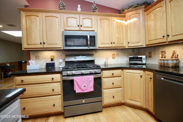 kitchen featuring appliances with stainless steel finishes, vaulted ceiling, light brown cabinets, and dark stone counters