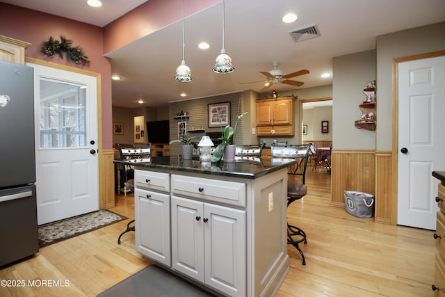 kitchen featuring stainless steel fridge, hanging light fixtures, a kitchen bar, light hardwood / wood-style floors, and a kitchen island