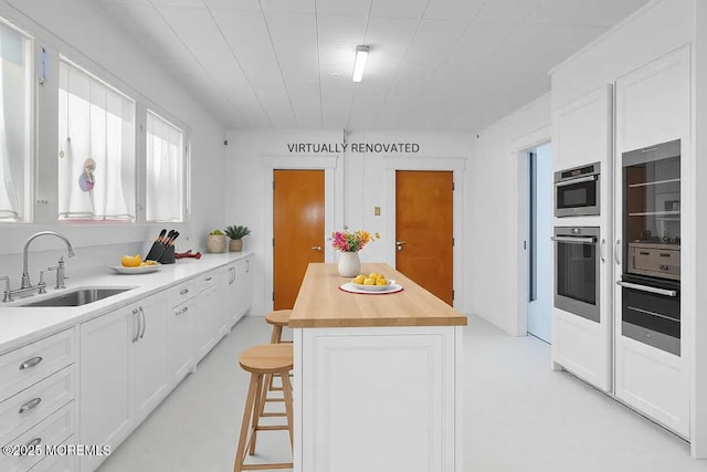 kitchen featuring sink, wooden counters, a kitchen island, white cabinets, and a kitchen bar