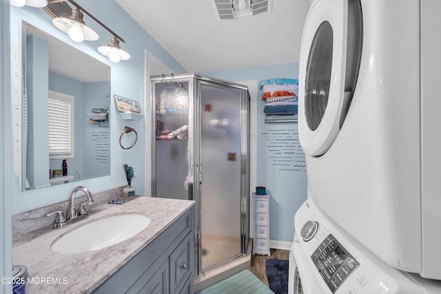 bathroom with vanity, a shower with door, and stacked washer and clothes dryer