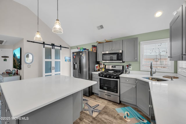 kitchen with lofted ceiling, gray cabinets, appliances with stainless steel finishes, a center island, and a barn door