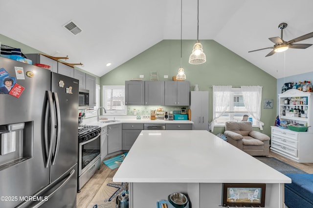 kitchen with lofted ceiling, gray cabinetry, a center island, appliances with stainless steel finishes, and light hardwood / wood-style floors