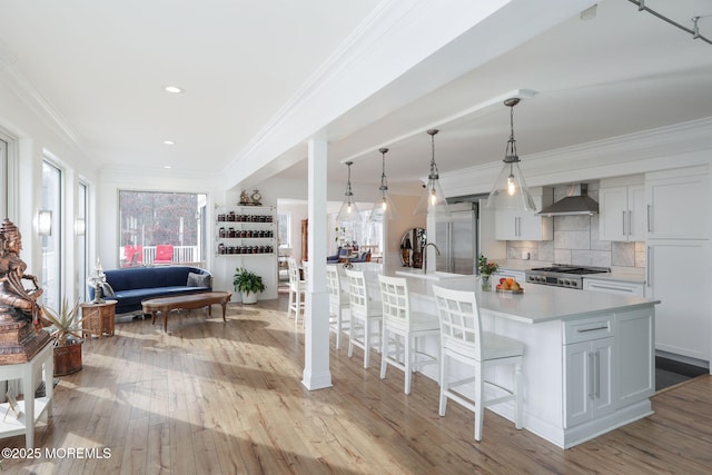 kitchen with wall chimney range hood, a spacious island, tasteful backsplash, a kitchen bar, and decorative light fixtures