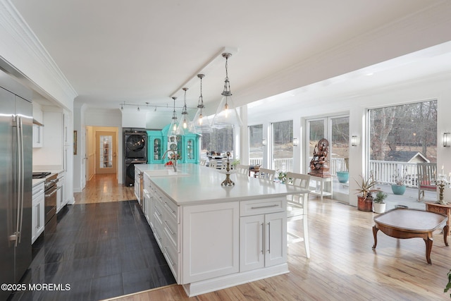 kitchen with pendant lighting, stacked washing maching and dryer, white cabinetry, premium appliances, and a center island with sink