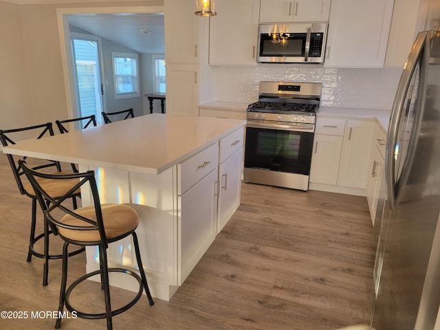 kitchen with appliances with stainless steel finishes, pendant lighting, white cabinetry, a kitchen bar, and a center island