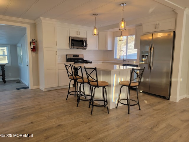 kitchen featuring appliances with stainless steel finishes, a kitchen breakfast bar, a center island, white cabinets, and decorative light fixtures