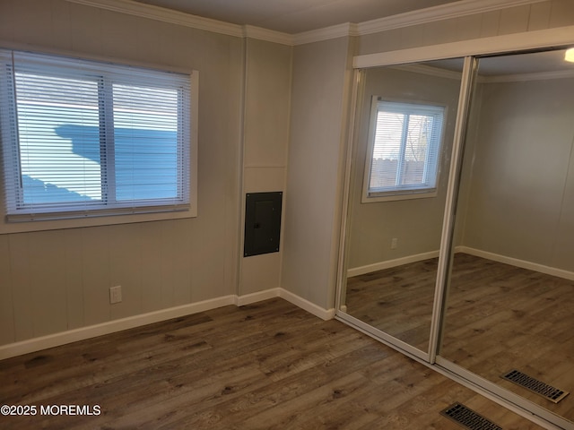 unfurnished bedroom with crown molding, electric panel, dark wood-type flooring, and a closet