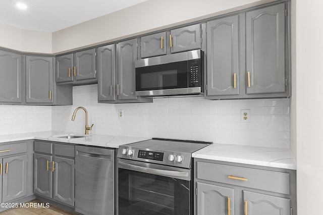 kitchen with sink, gray cabinetry, stainless steel appliances, light stone counters, and decorative backsplash