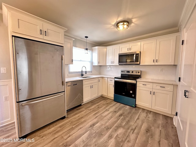 kitchen with sink, crown molding, hanging light fixtures, stainless steel appliances, and white cabinets