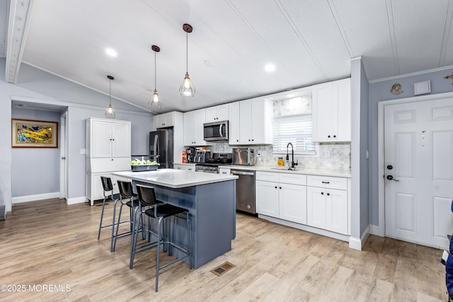 kitchen featuring pendant lighting, lofted ceiling, appliances with stainless steel finishes, white cabinetry, and a kitchen island