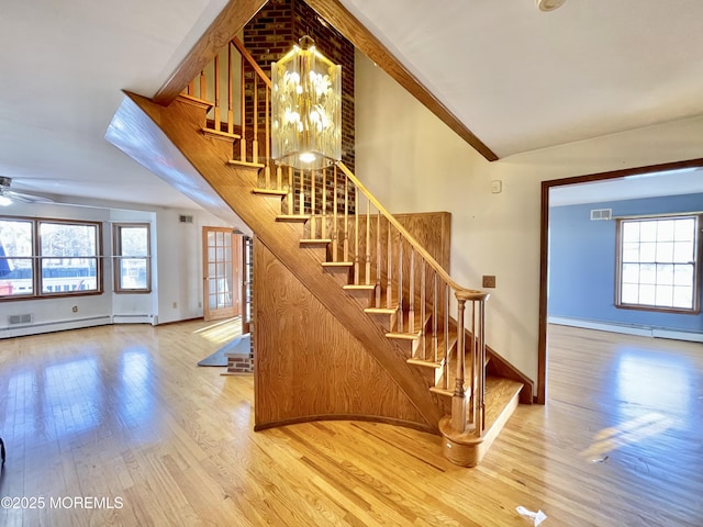 stairway featuring vaulted ceiling, baseboard heating, ceiling fan with notable chandelier, and hardwood / wood-style floors