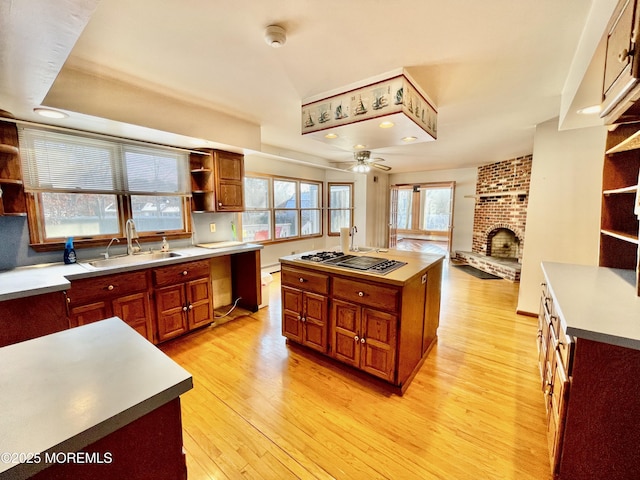 kitchen with a kitchen island, a fireplace, sink, stainless steel gas cooktop, and light wood-type flooring