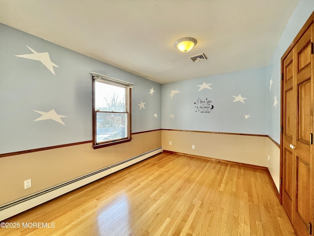 unfurnished room with a baseboard heating unit and light hardwood / wood-style floors