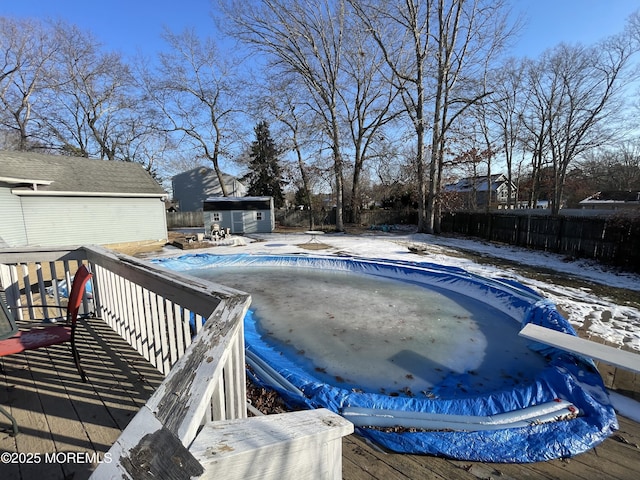 snow covered pool with a wooden deck, a diving board, and a shed