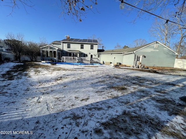 snow covered house featuring a sunroom and solar panels