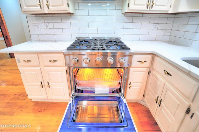 705 Princeton Rd, Lanoka Harbor, NJ 08734 - kitchen featuring wood finished floors, white cabinets, decorative backsplash, light stone counters, and stainless steel gas range