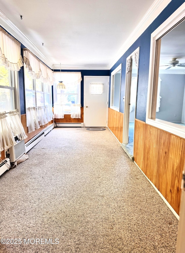 empty room featuring a baseboard heating unit, crown molding, wooden walls, and carpet flooring