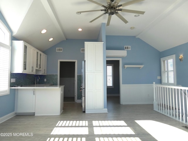 kitchen featuring lofted ceiling, sink, white cabinetry, light hardwood / wood-style flooring, and decorative backsplash