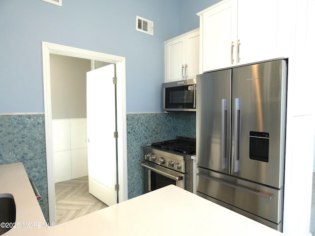 kitchen featuring tile walls, light parquet floors, white cabinets, and appliances with stainless steel finishes