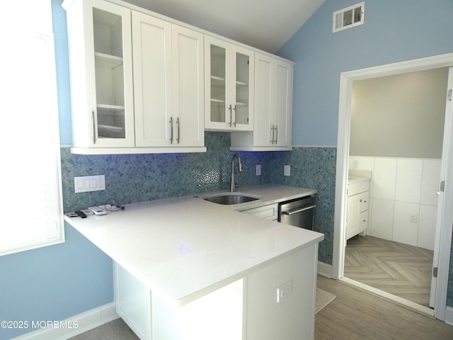 kitchen featuring lofted ceiling, sink, white cabinets, stainless steel dishwasher, and kitchen peninsula