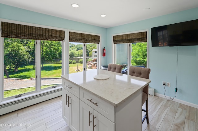 kitchen featuring a baseboard heating unit, white cabinets, light stone countertops, light wood finished floors, and a kitchen bar