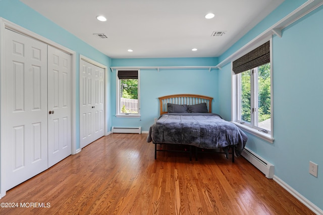 bedroom with a baseboard heating unit, wood finished floors, two closets, and visible vents