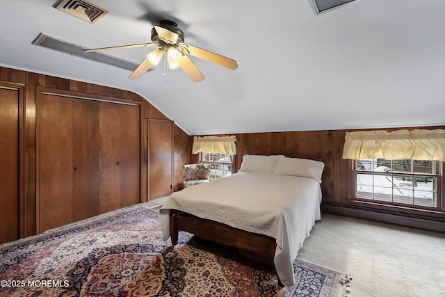 carpeted bedroom featuring ceiling fan, baseboard heating, vaulted ceiling, a closet, and wood walls