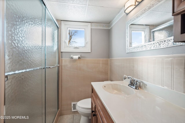 bathroom featuring a paneled ceiling, a shower with door, tile patterned flooring, vanity, and toilet