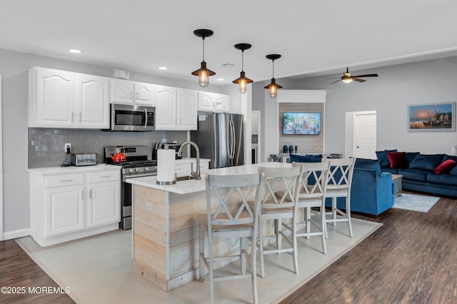 kitchen with an island with sink, appliances with stainless steel finishes, white cabinets, and decorative light fixtures