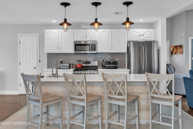 kitchen featuring appliances with stainless steel finishes, white cabinets, a kitchen bar, decorative backsplash, and hanging light fixtures